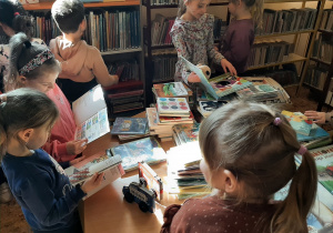 Przy stoliku w bibliotece grupa przedszkolakówogląda książki dla dzieci.