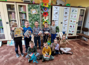 Dzieci z grupy stoją w grupie w bibliotece z książkami i pluszowymi dinozaurami