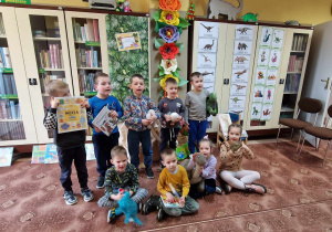Grupowe zdjęcie dzieci w bibliotece. W tle dekoracja z ilustracjami dinozaurów
