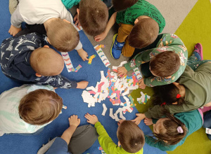Dzieci w kole na dywanie układają kolorowe papierowe skarpety