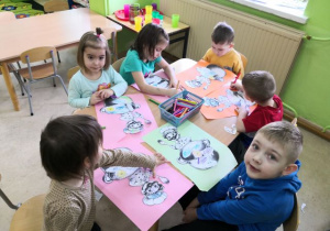 Przedszkolaki siedzą przy stoliku i wykonują pracę plastyczną "Marcowa pogoda".