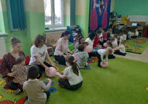 Dzieci wspólnie z mamami bawią się na dywanie balonami.