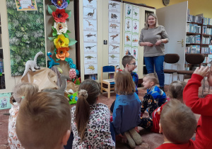 Dzieci w bibliotece słuchają opowieści pani bibliotekarki o dinozaurach.