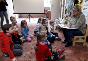 Dzieci w bibliotece słuchają opowieści pani bibliotekarki o dinozaurach.