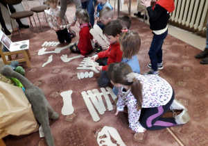 Dzieci układają szkielet dinozaura z wielu elementów.