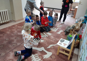Dzieci układają szkielet dinozaura z wielu elementów.