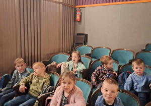 Dzieci siedzą na fotelach i czekają na spektakl.