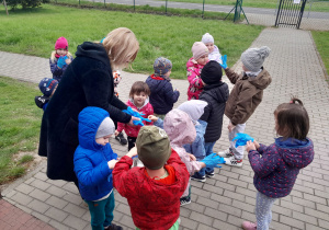 Dzieci zakładają rękawiczki ochronne, przygotowują się do porządkowania terenu wokół przedszkola.