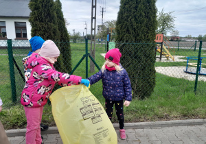 Dzieci zbierają śmieci i wrzucają do odpowiednich worków.