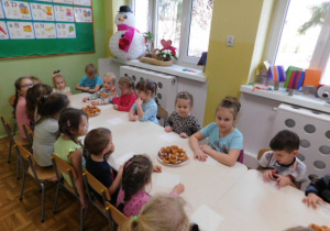 Dzieci siedzące przy stoliku i kosztujące własnoręcznie wykonane oponki