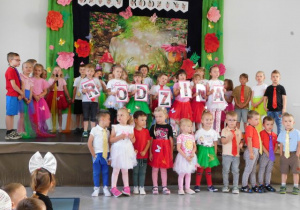 Przedszkolaki występują na scenie na tle bajkowej scenerii, trzymają napis rodzina.