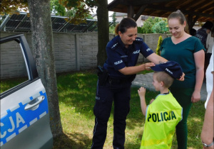 Dziecko wraz z rodzicem stoi przy radiowozie z policjantką.