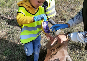 w lesie - chłopiec wrzuca do plastikowego worka znaleziony odpadek.