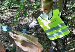 Chłopiec umieszcza w worku na śmieci plastikowy odpadek.