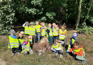 Dzieci podczas udziału w akcji sprzątanie świata w pobliskim lesie, pozują do fotografii. Stoją przy workach z zebranymi śmieciami.