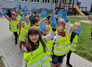 Dzieci w kamizelkach, rękawiczkach z workami stoją przed budynkiem przedszkolnym