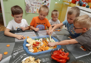 Kilku chłopców przy stoliku układa części warzyw tworząc warzywne obrazki.