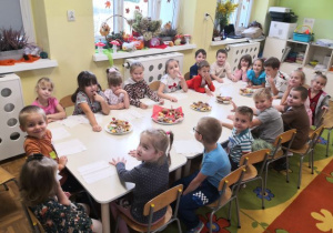 Przedszkolaki siedzą przy stole i częstują się babeczkami.