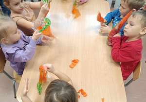 Dzieci podczas pracy plastycznej siedzą przy stolikach.