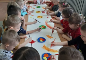 Dzieci siedzą przy stolikach i malują farbami.