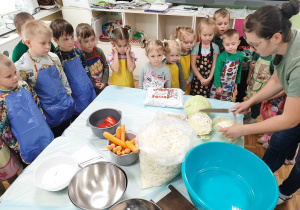 Dzieci ustawione wokół stołu patrzą jak rodzic kroi kapustę.