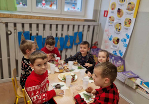 Dzieci siedzą przy stoliku zastawionym słodyczami.