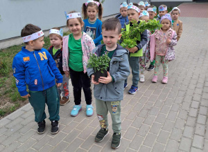 Dzieci w grupie przed przedszkolem trzymają rośliny do wsadzenia