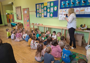 Dzieci siedzą na holu przedszkolnym i słuchają nauczyciela