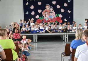 Dzieci siedzą na scenie i przygotowują się do występu z okazji Dnia Rodziny