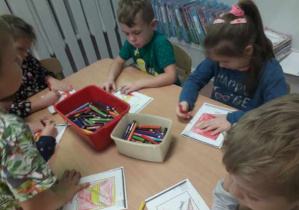 Dzieci przy stoliku kolorują rysunek.