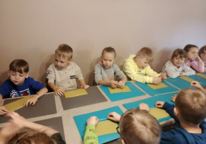 Dzieci siedzą przy stole i wykonują świecę z plastra wosku pszczelego.