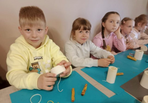 Dzieci siedzą przy stoliku i wykonują świece z użyciem silikonowych form.