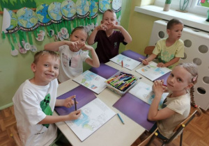 Przedszkolaki siedzą przy stoliku i wykonują karty pracy.