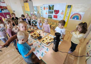 Przedszkolaki stoją dookoła stołu, na którym stoją przygotowane owoce.