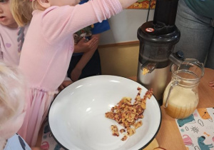 Dziewczynka wkłada owoce do wyciskarki soków.