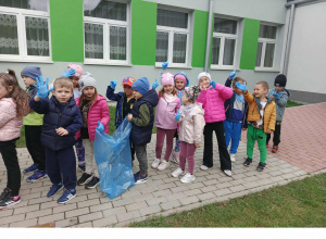 Dzieci w grupie z workami i rękawiczkami przed budynkiem przedszkola