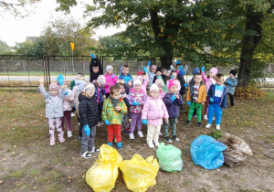 Dzieci w grupie na boisku przedszkolnym. Przed nimi leżą worki z zebranymi śmieciami.