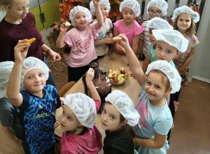 Dzieci stoją z owocami przy stole na którym jest sokowirówka