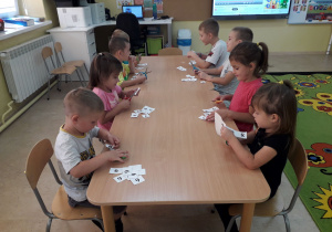 Dzieci przy stoliku wycinają cyfry i układają z nich numery alarmowe.