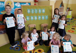 Dzieci pozują do zdjęcia z dyplomami na tle napisu Dzień Kropki.