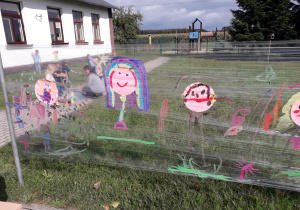 Namalowane portrety dzieci w plenerowej strefie kreatywności.