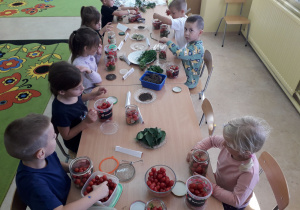 Dzieci przy stolikach kiszą pomidorki.