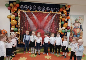 Grupa młodsza stoi w półkolu na tle dekoracji i śpiewa piosenkę.