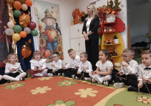 Dzieci siedzą na dywanie i grają na instrumentach.