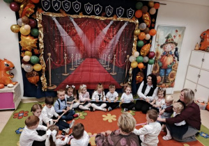 Przedszolaki siedzą w kole z paniami i prezentują zabawę z gumą sensoryczną.