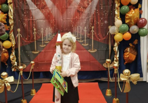 Dziewczynka pozuje do zdjęcia na czerownym dywanie.