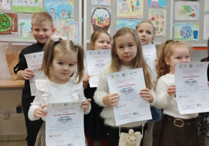 Laureaci konkursu pozują do zdjecia z dyplomami na tle prac konkursowych