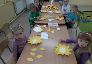 Dzieci przy stoliku podczas zajęć plastycznych wykonują jesienne kwiaty - słoneczniki.
