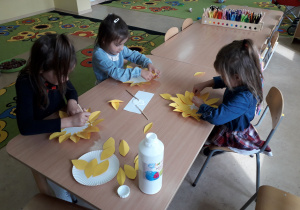 Dziewczynki przy stoliku wykonują jesienne kwiaty- słoneczniki.