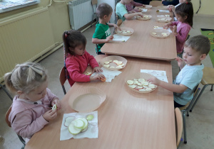 Dzieci przy stoliku wykonują susz jabłkowy, układają plastry jabłek na pergaminie.